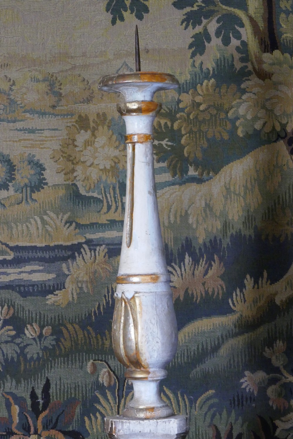A carved 19th-century wooden pricket candlestick featuring distressed off-white paint, exposed gold leafing, an acanthus column motif, and an iron candle spike. View V