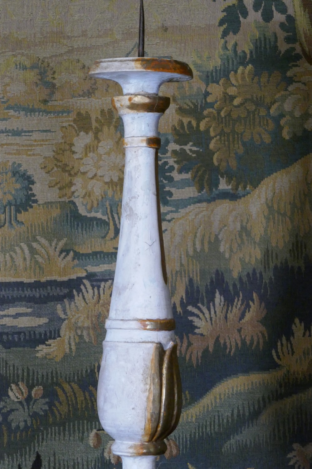 A carved 19th-century wooden pricket candlestick featuring distressed off-white paint, exposed gold leafing, an acanthus column motif, and an iron candle spike. View VIII