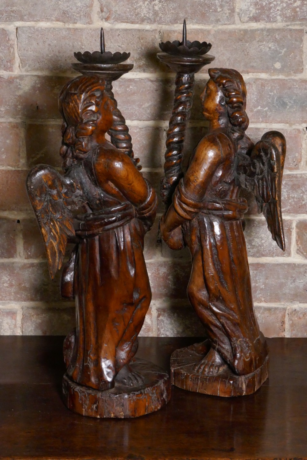 A pair of antique hand-carved wooden candlesticks depicting standing winged angels holding barley-twist pricket stands.