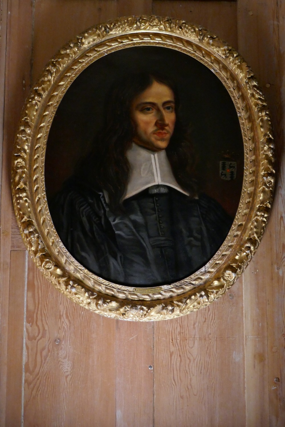 An antique oval oil painting depicting a gentleman in dark clothing and a white collar, framed in an ornate gilded carved frame.