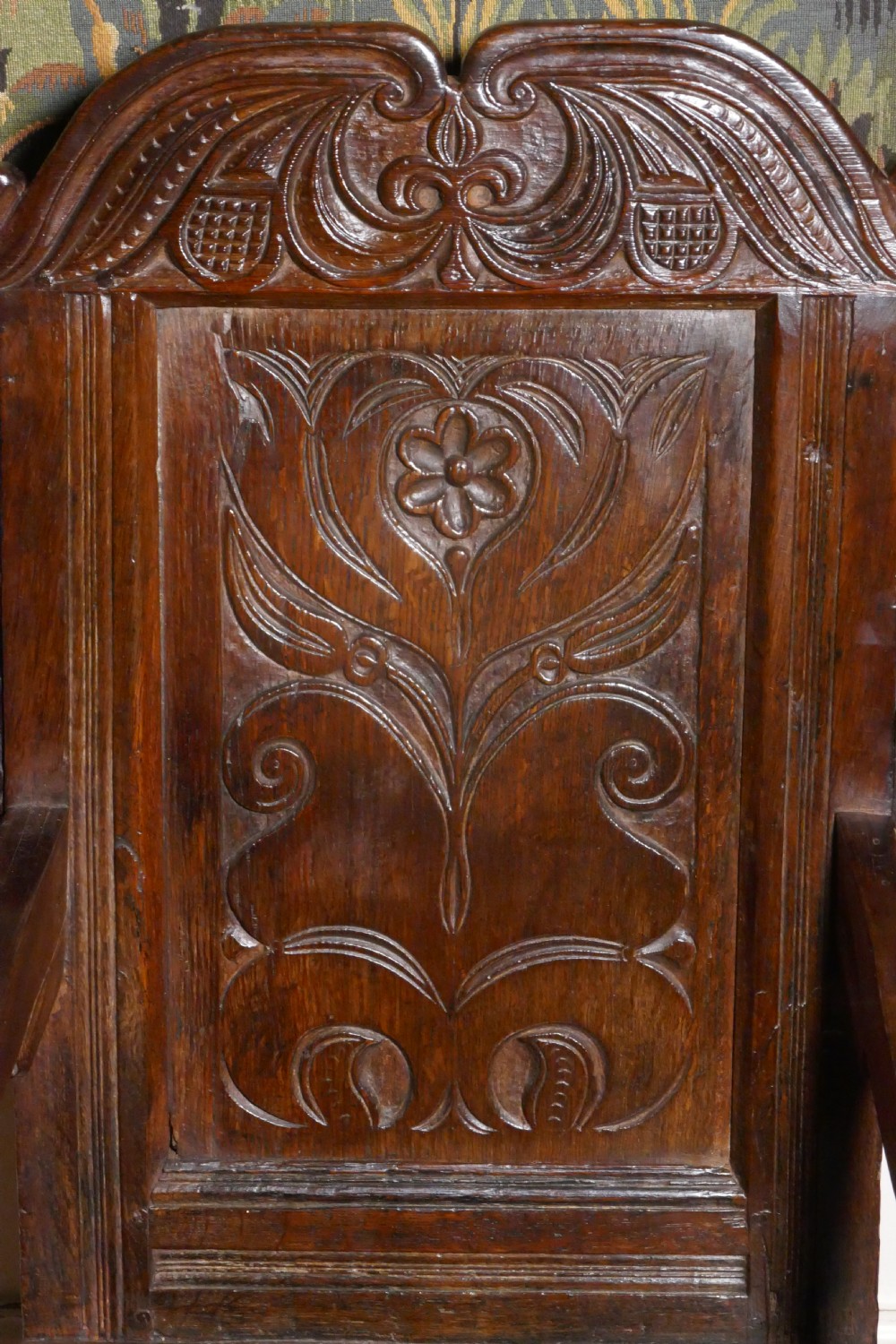 A 17th-century dark oak wainscot chair with a carved floral panel, arched cresting rail, and turned front legs. View II