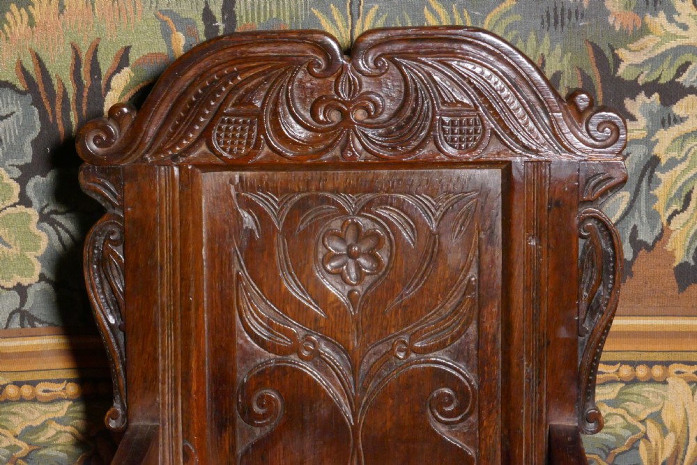 A 17th-century dark oak wainscot chair with a carved floral panel, arched cresting rail, and turned front legs. View III
