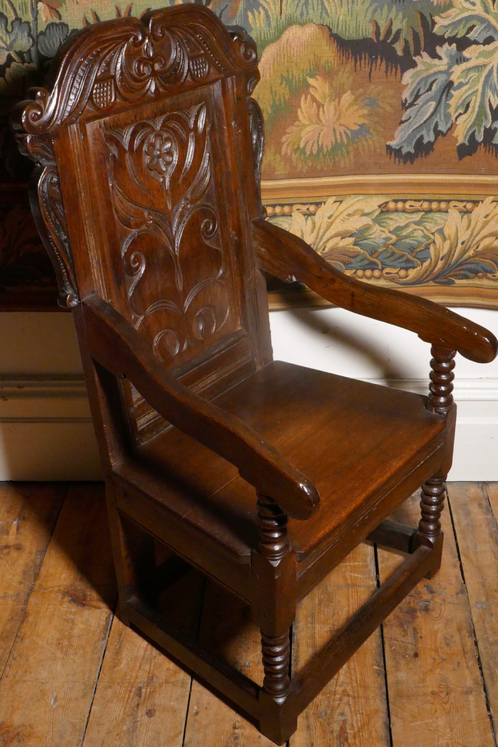 A 17th-century dark oak wainscot chair with a carved floral panel, arched cresting rail, and turned front legs. View IV