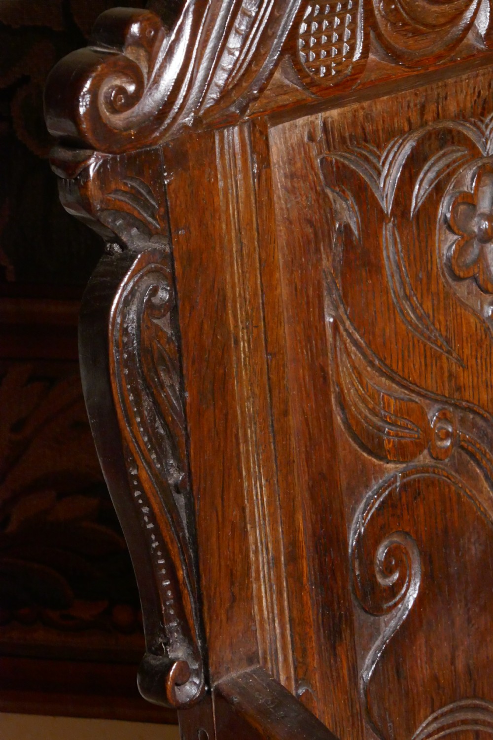 A 17th-century dark oak wainscot chair with a carved floral panel, arched cresting rail, and turned front legs. View V