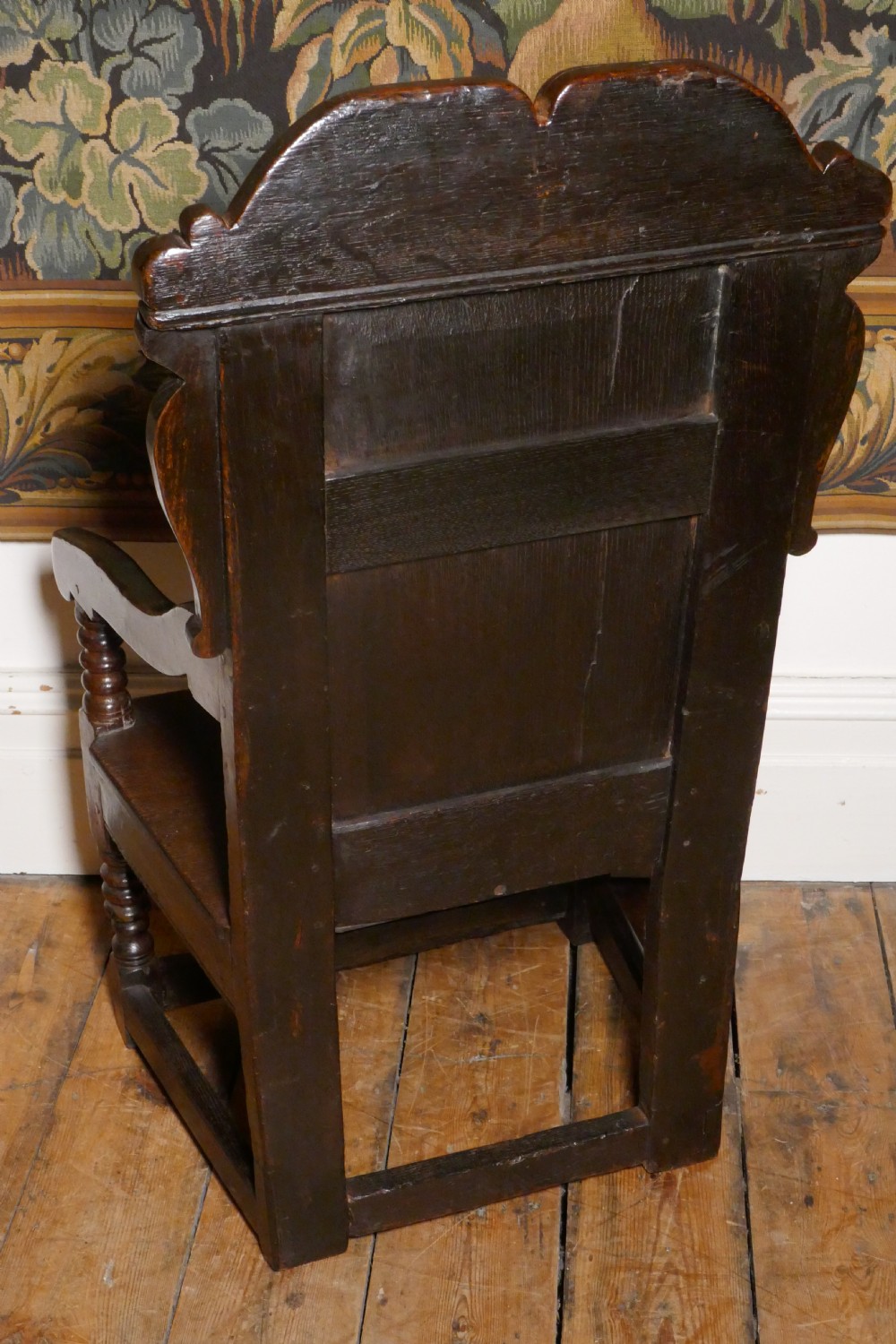 A 17th-century dark oak wainscot chair with a carved floral panel, arched cresting rail, and turned front legs. View VIII