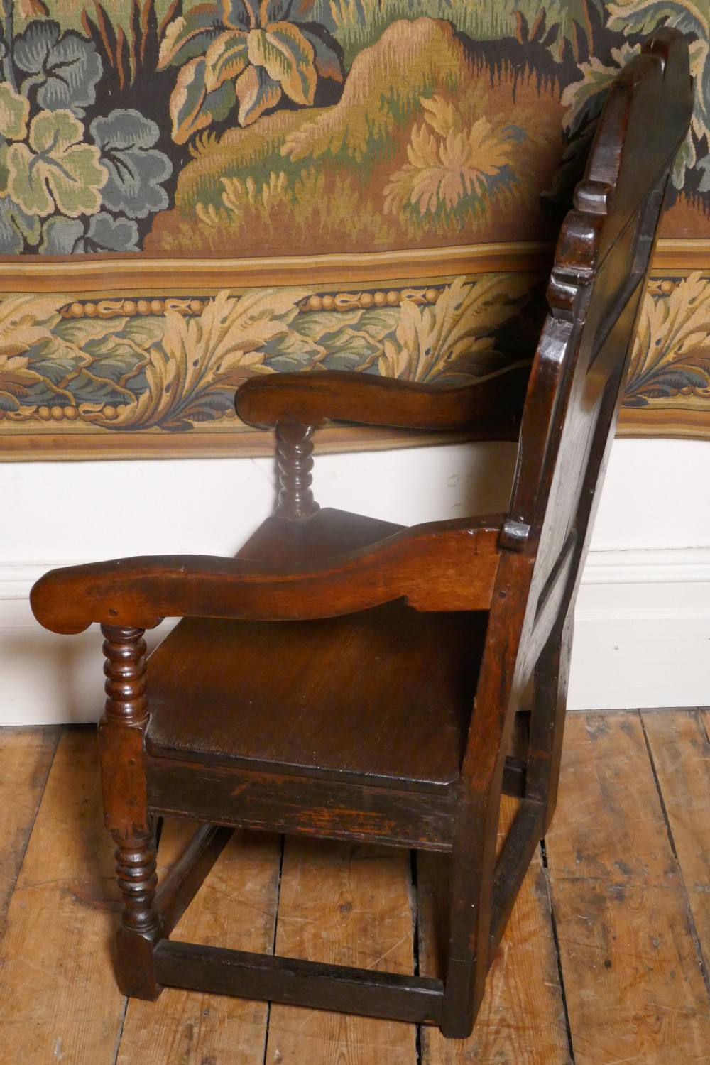 A 17th-century dark oak wainscot chair with a carved floral panel, arched cresting rail, and turned front legs. View IX