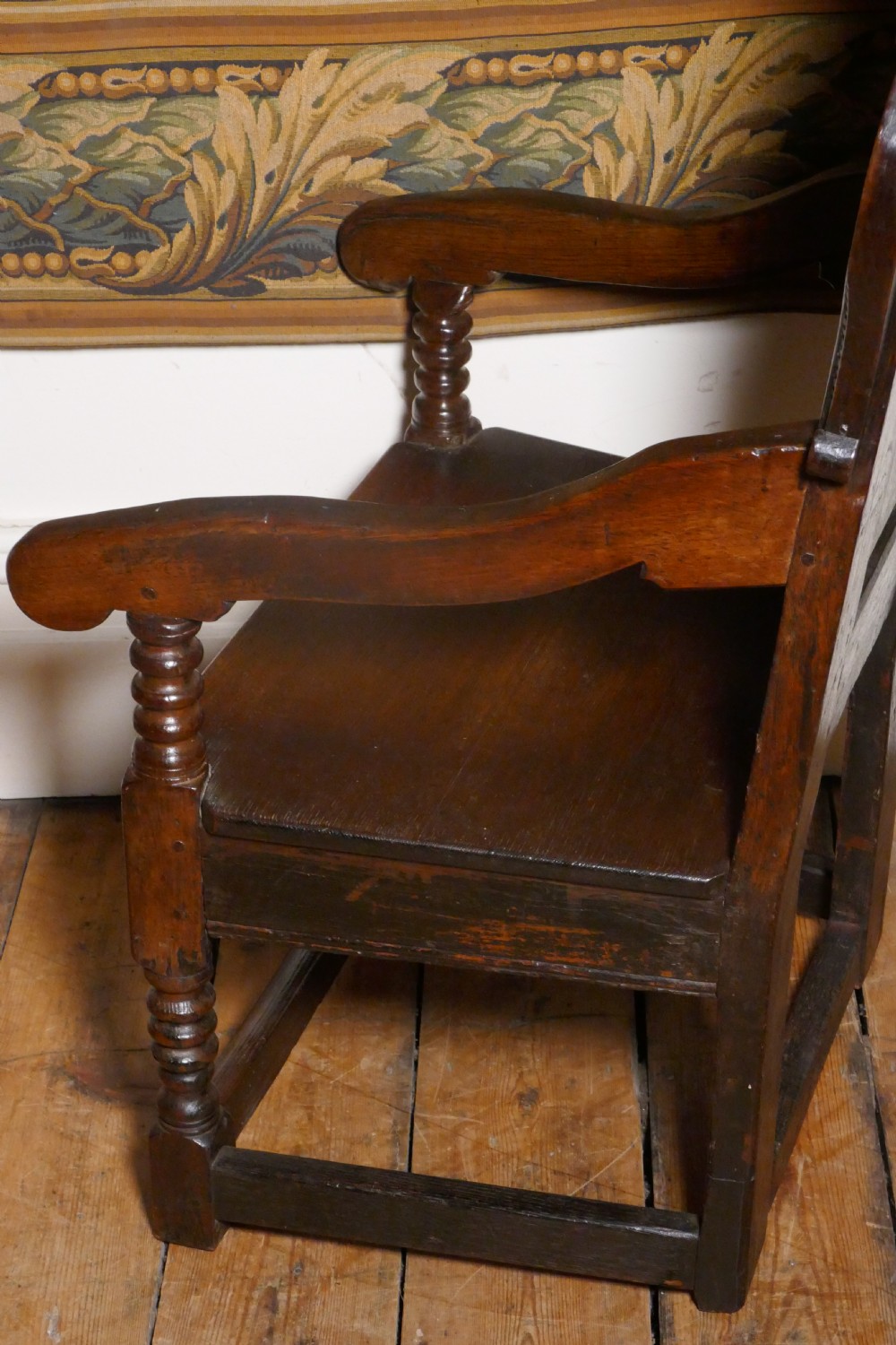 A 17th-century dark oak wainscot chair with a carved floral panel, arched cresting rail, and turned front legs. View X