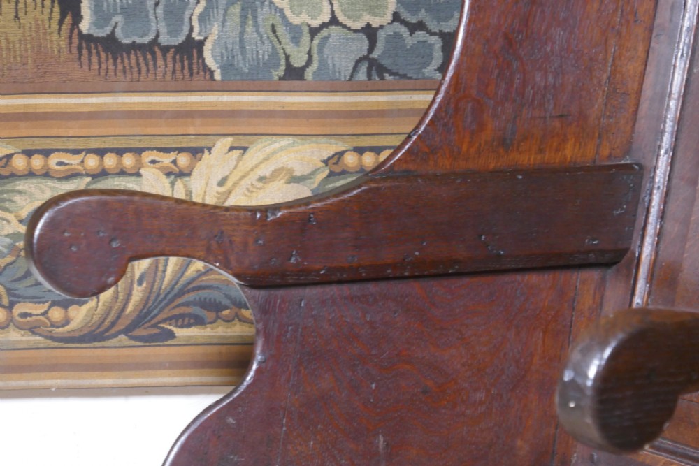 A solid dark oak Georgian wing back armchair featuring a fielded panel back, shaped armrests, and turned front legs connected by stretchers. View X