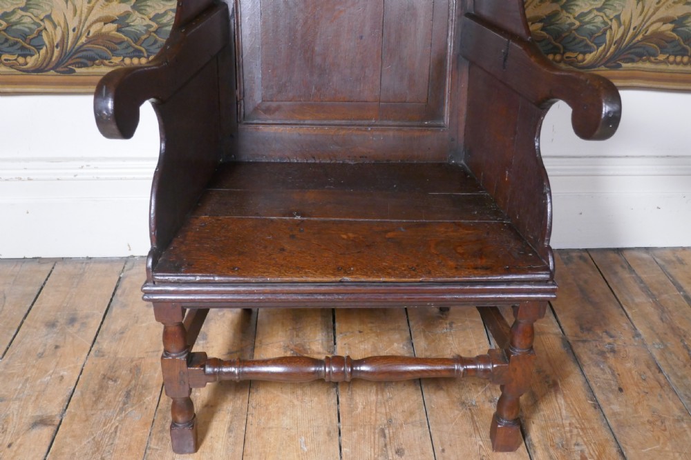 A solid dark oak Georgian wing back armchair featuring a fielded panel back, shaped armrests, and turned front legs connected by stretchers. View XI