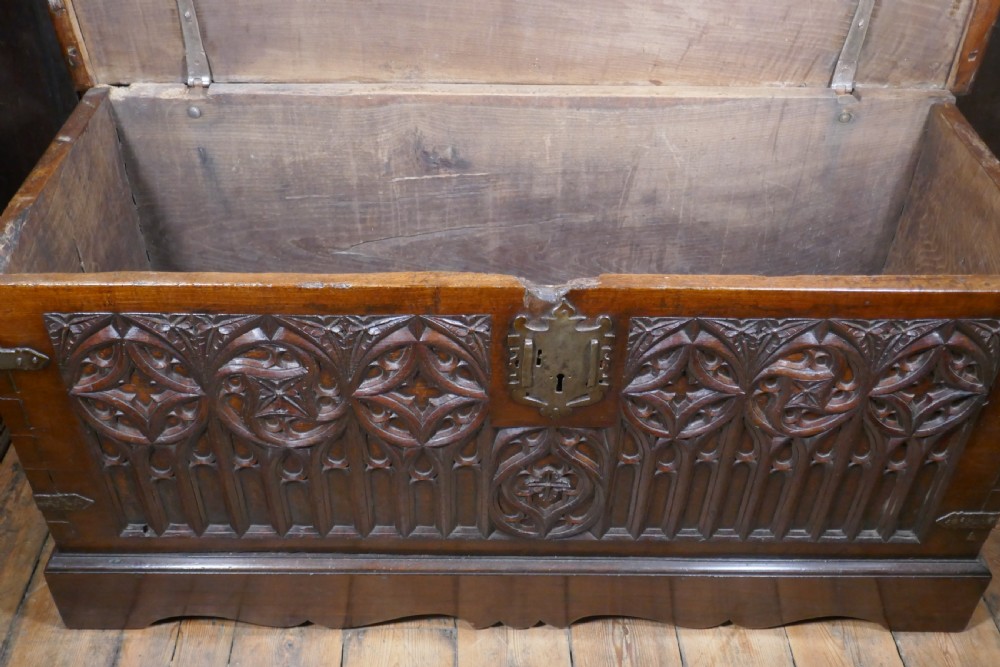 A dark oak 16th-century coffer featuring carved Gothic tracery panels and a central iron lock mechanism. View V