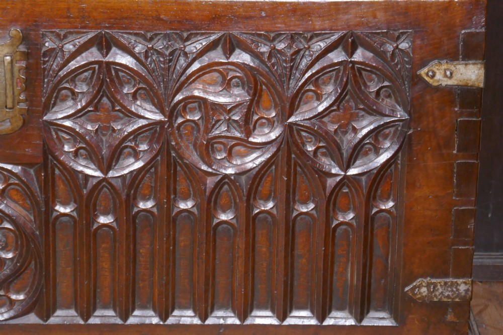 A dark oak 16th-century coffer featuring carved Gothic tracery panels and a central iron lock mechanism. View X