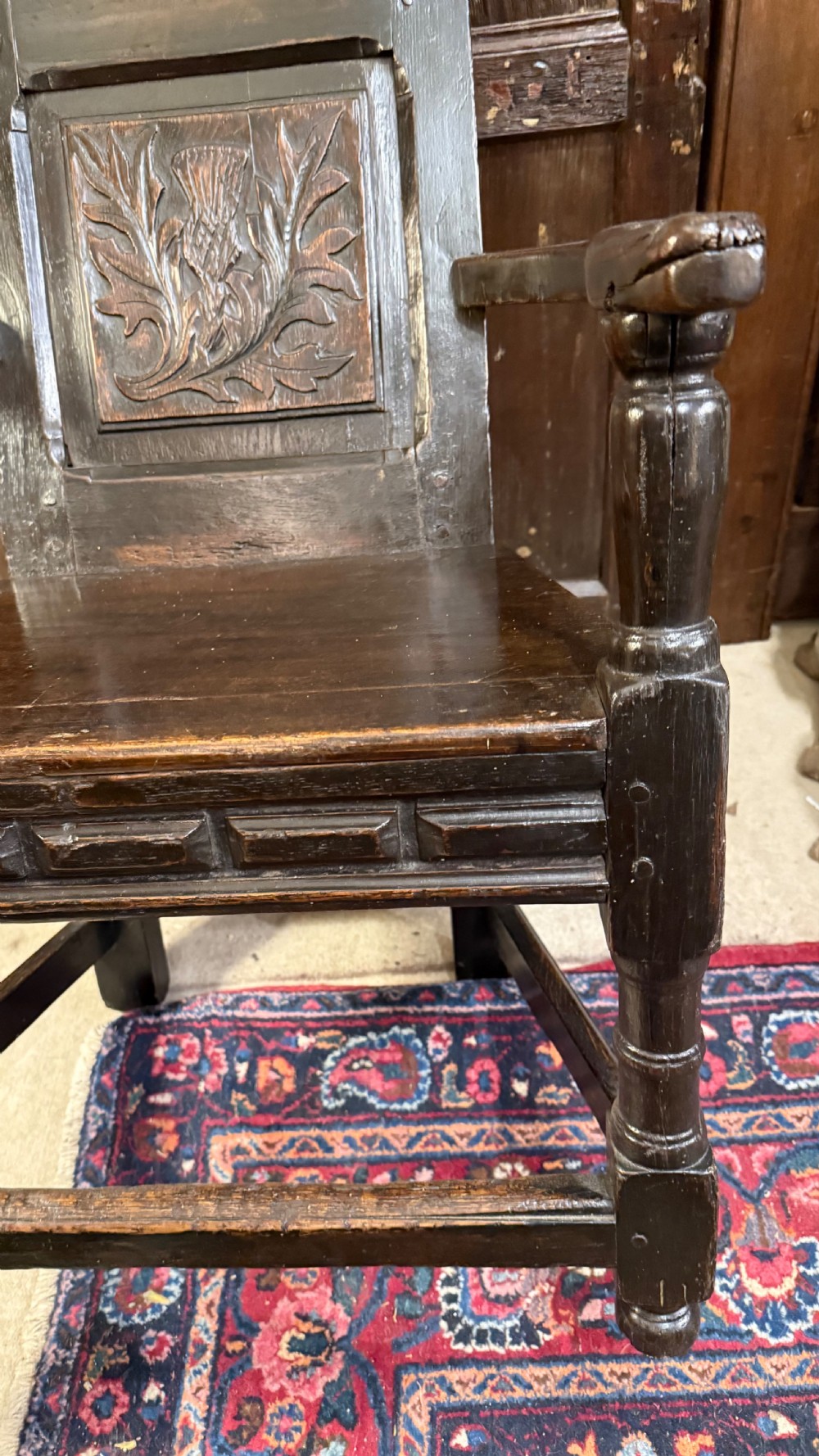 A 17th-century dark oak wainscot armchair with a carved thistle back panel, carved top crest, and turned legs. View VI