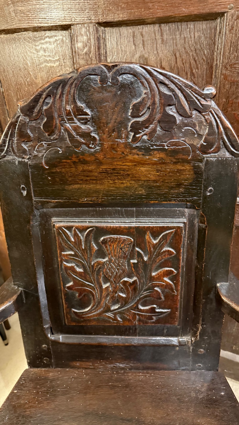 A 17th-century dark oak wainscot armchair with a carved thistle back panel, carved top crest, and turned legs. View VIII