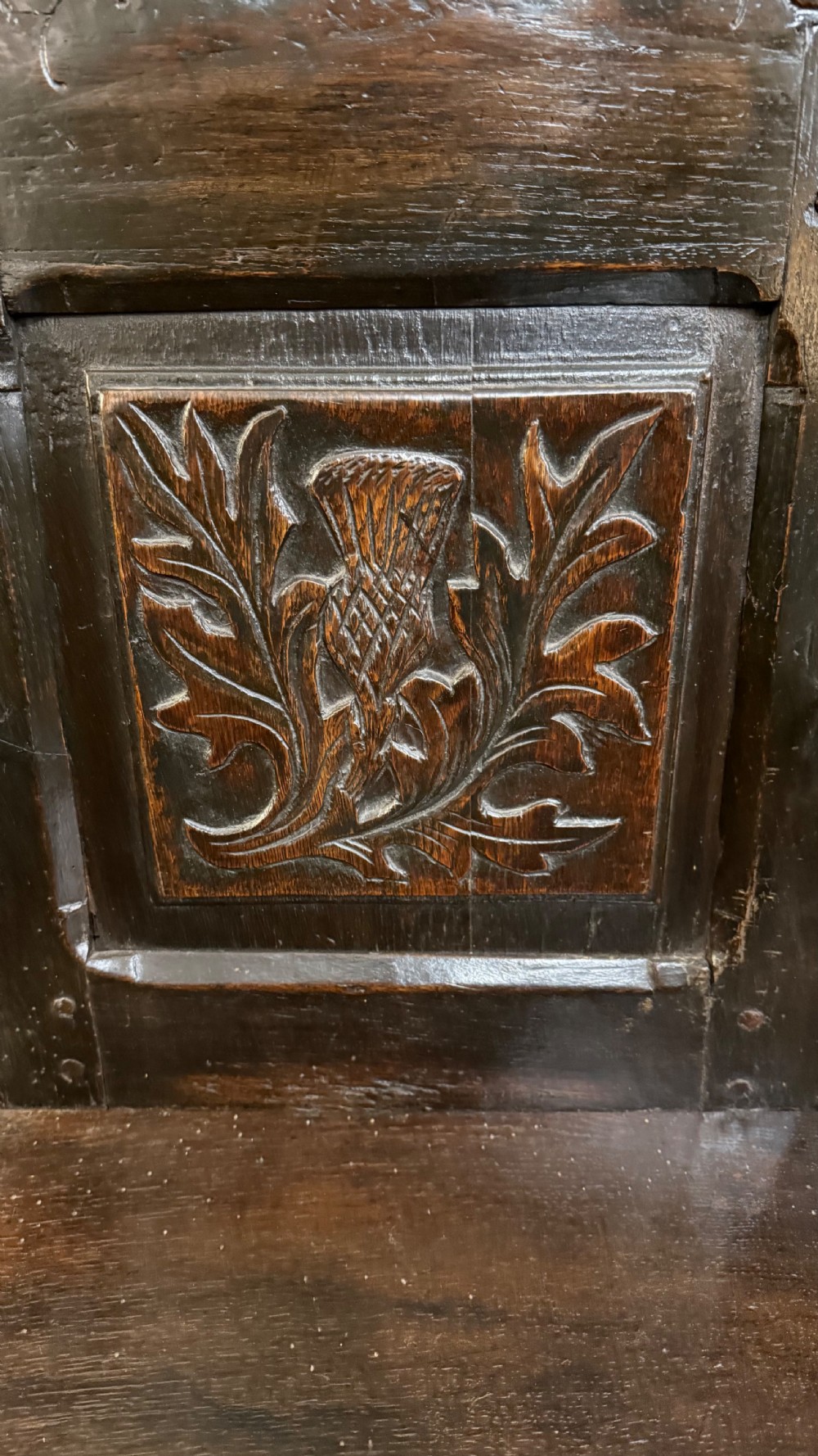 A 17th-century dark oak wainscot armchair with a carved thistle back panel, carved top crest, and turned legs. View IX