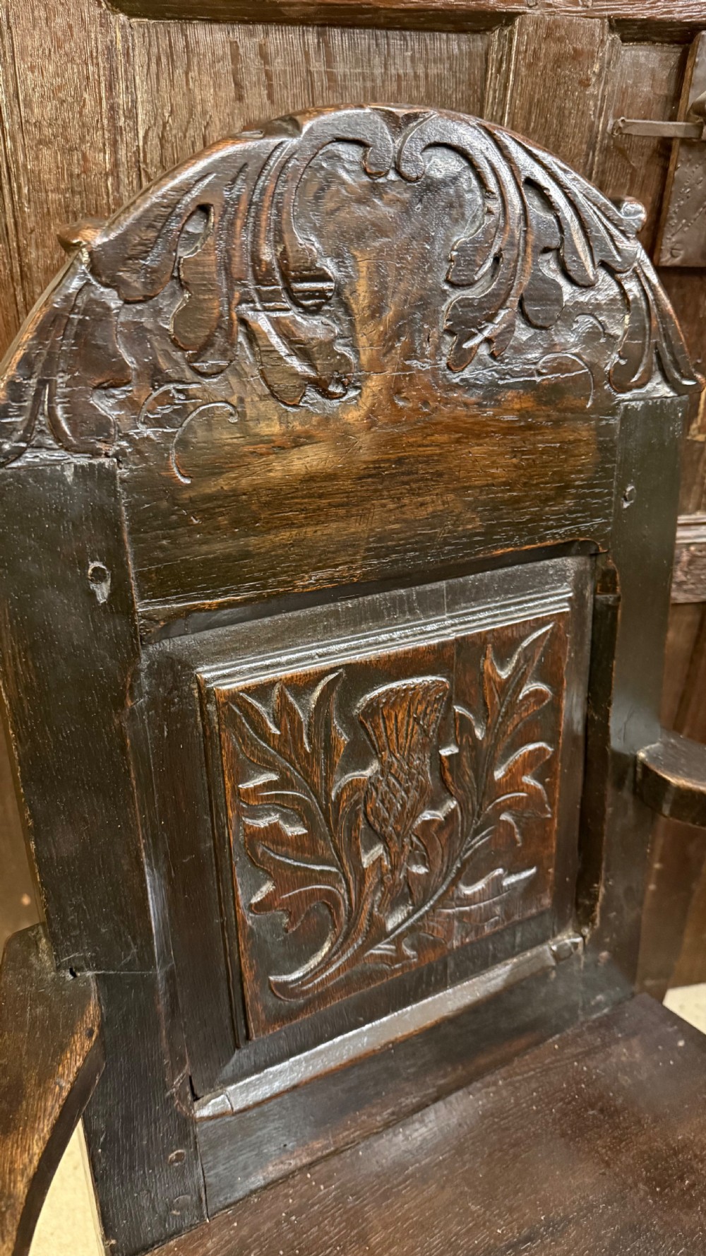 A 17th-century dark oak wainscot armchair with a carved thistle back panel, carved top crest, and turned legs. View XIII
