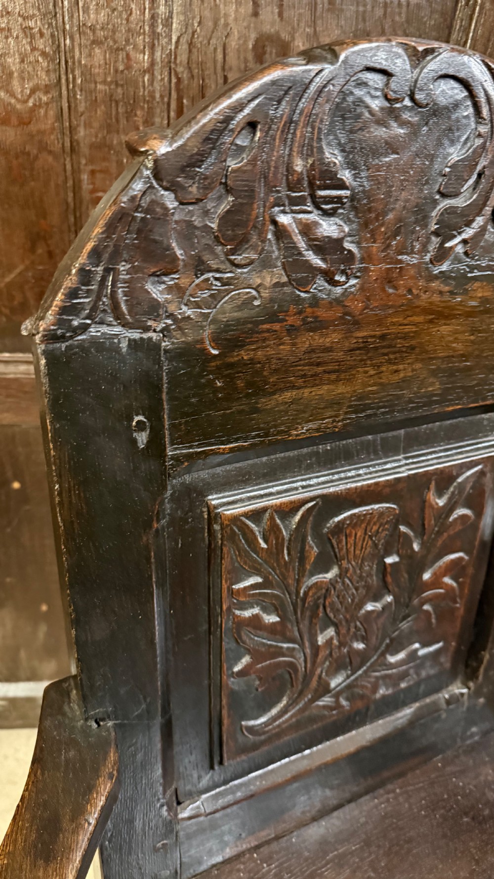 A 17th-century dark oak wainscot armchair with a carved thistle back panel, carved top crest, and turned legs. View XVI