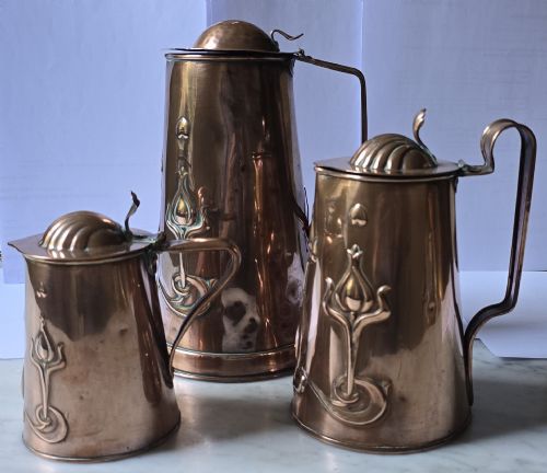 fig 1. A set of three graduated copper jugs featuring embossed Art Nouveau floral motifs and shell-shaped hinged lids.