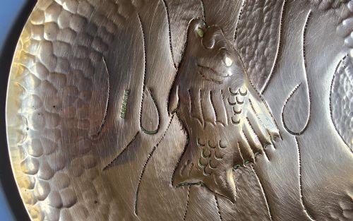 fig 2. A circular hand-hammered copper visiting card tray featuring a central repousse fish motif surrounded by chased water lines and a spot-hammered rim.
