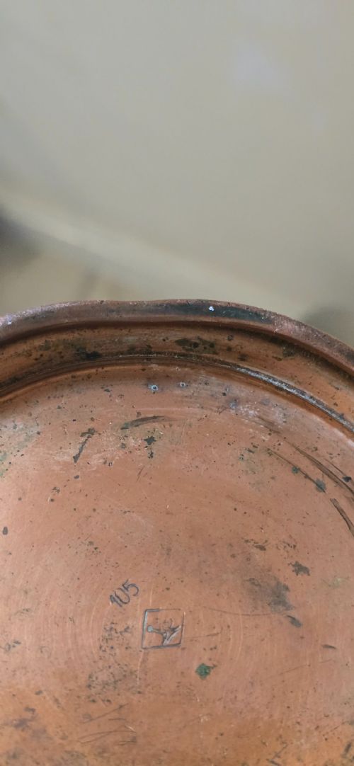 fig 2. An Art Nouveau tapered copper ewer with a raised floral relief pattern, angular brass handle, hinged brass cap, and subtle dark circular motifs near the base.