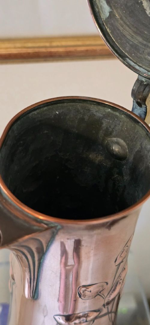 An Art Nouveau tapered copper ewer with a raised floral relief pattern, angular brass handle, hinged brass cap, and subtle dark circular motifs near the base. View X