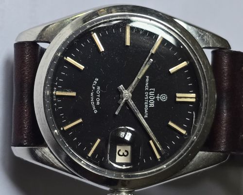 fig 4. A vintage Tudor Prince Oysterdate wristwatch with a stainless steel case, a black dial featuring baton hour markers, a date aperture at three oclock, and a dark brown leather strap.