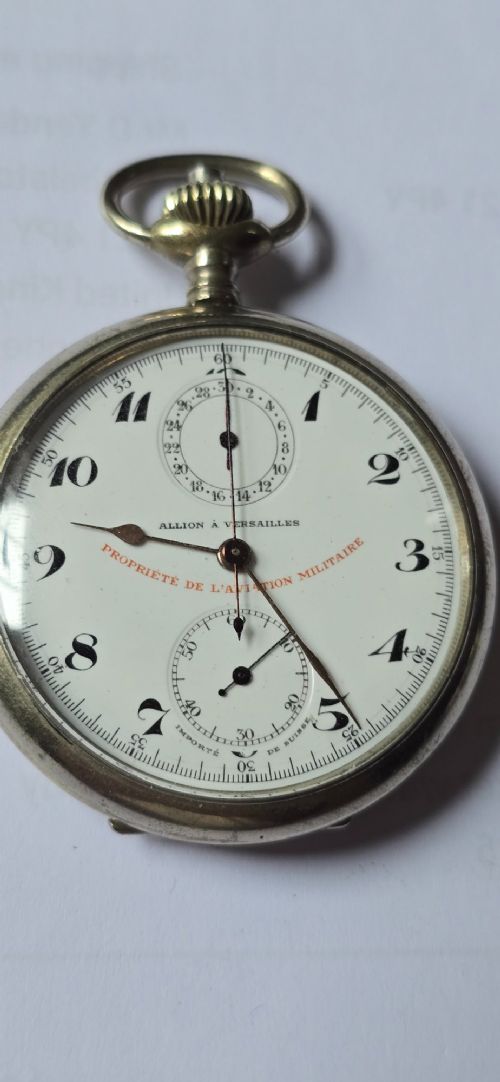 fig 1. An open-face military pocket watch chronograph featuring a white enamel dial with black Arabic numerals, dual sub-dials, and French military markings enclosed in a round silver case.