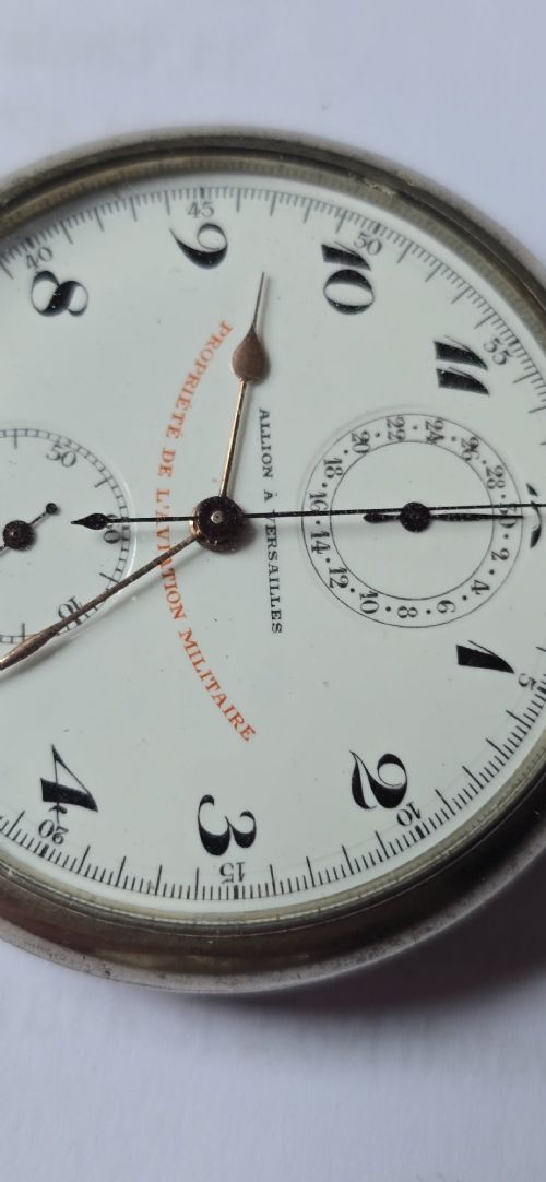 fig 2. An open-face military pocket watch chronograph featuring a white enamel dial with black Arabic numerals, dual sub-dials, and French military markings enclosed in a round silver case.