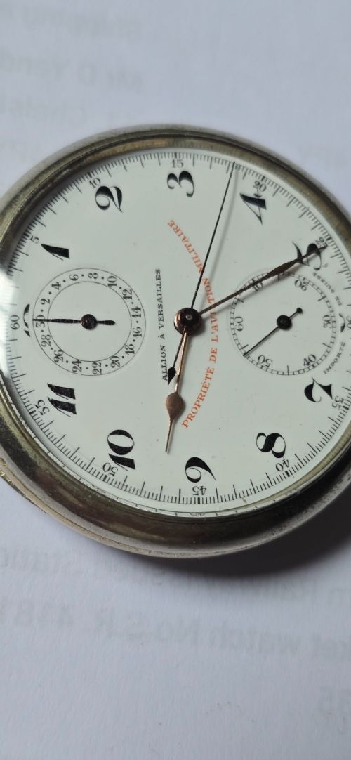 fig 3. An open-face military pocket watch chronograph featuring a white enamel dial with black Arabic numerals, dual sub-dials, and French military markings enclosed in a round silver case.