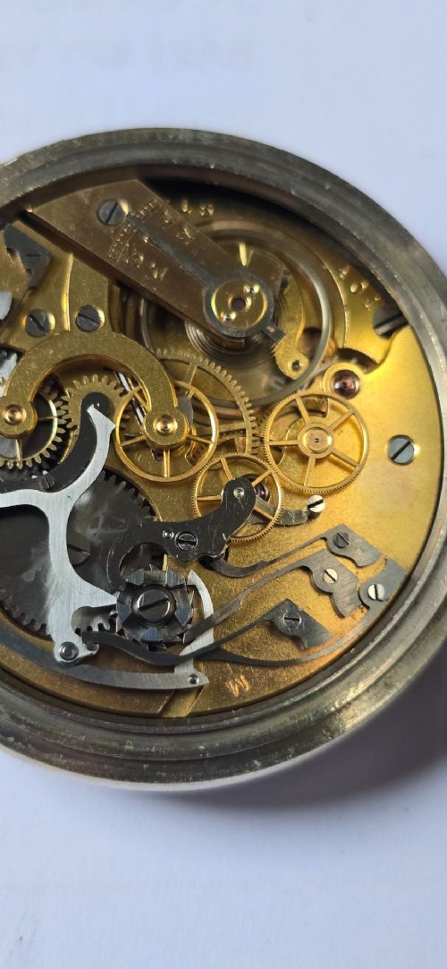 fig 7. An open-face military pocket watch chronograph featuring a white enamel dial with black Arabic numerals, dual sub-dials, and French military markings enclosed in a round silver case.