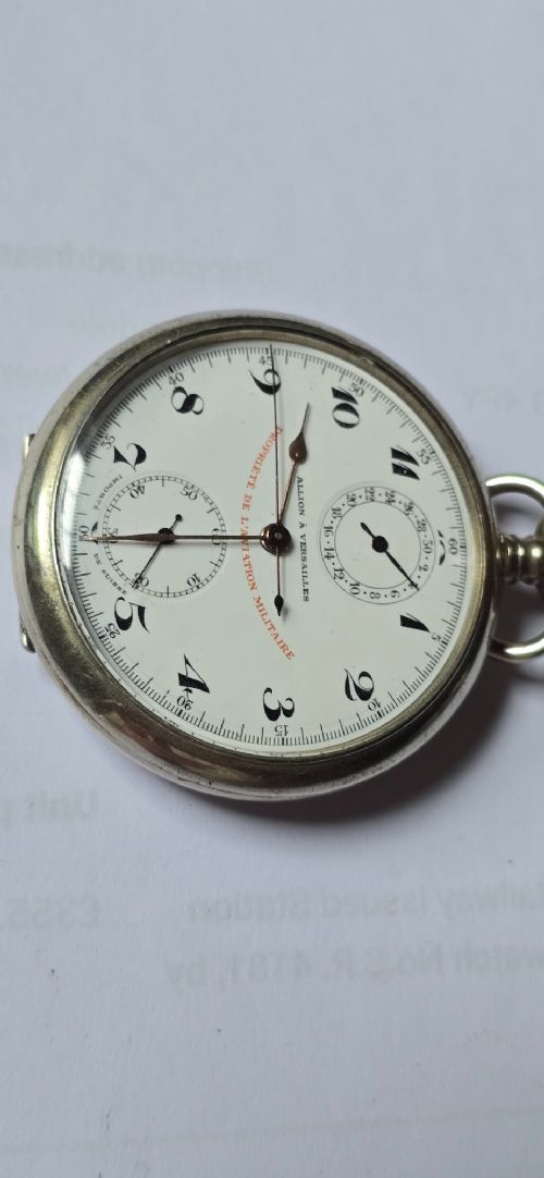 fig 8. An open-face military pocket watch chronograph featuring a white enamel dial with black Arabic numerals, dual sub-dials, and French military markings enclosed in a round silver case.