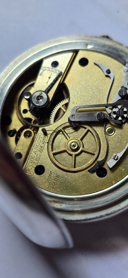 fig 7. An open-face silver pocket watch featuring a white enamel dial with black Roman numerals, split-seconds hands, a subsidiary seconds dial, and a brass onion crown at the top.