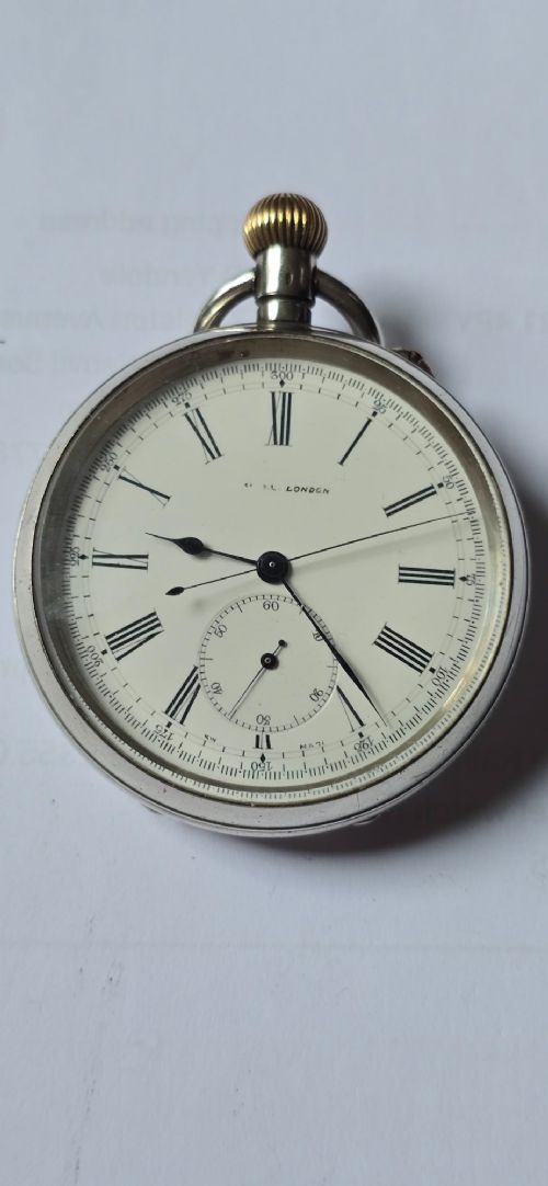An open-face silver pocket watch featuring a white enamel dial with black Roman numerals, split-seconds hands, a subsidiary seconds dial, and a brass onion crown at the top. View IX