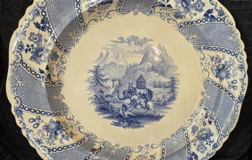 fig 1. An antique circular earthenware plate featuring a blue transfer-printed central scene of Hannibal with an elephant and figures in a mountainous landscape, surrounded by an ornate scalloped floral border.