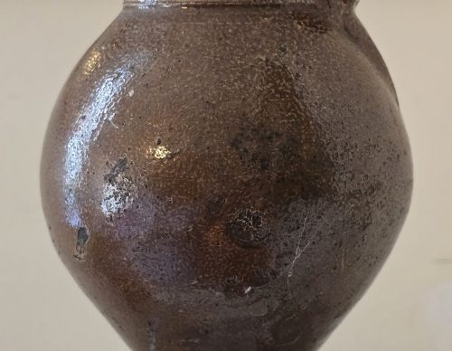 fig 6. A 17th-century dark brown salt-glazed stoneware bottle featuring a bulbous body, narrow neck, turned base, and a single loop handle.