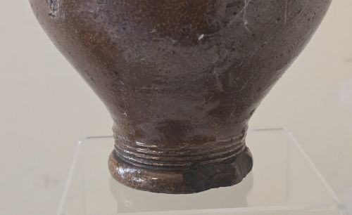fig 7. A 17th-century dark brown salt-glazed stoneware bottle featuring a bulbous body, narrow neck, turned base, and a single loop handle.