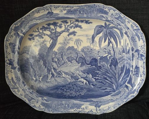 fig 2. An oval blue and white underglaze transfer-printed earthenware meat platter depicting a landscape with hunters on elephants and hounds pursuing a leopard.
