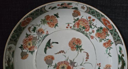 fig 1. A circular Chinese famille verte porcelain dish featuring hand-painted peony blossoms, foliage, a bird in flight, and a decorative patterned border.