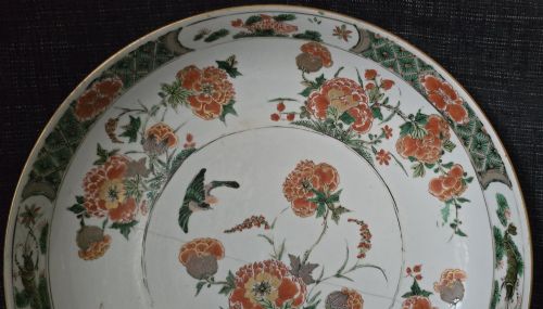 fig 4. A circular Chinese famille verte porcelain dish featuring hand-painted peony blossoms, foliage, a bird in flight, and a decorative patterned border.