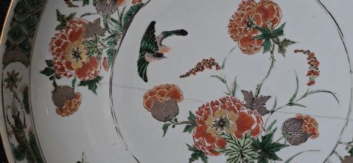 fig 5. A circular Chinese famille verte porcelain dish featuring hand-painted peony blossoms, foliage, a bird in flight, and a decorative patterned border.