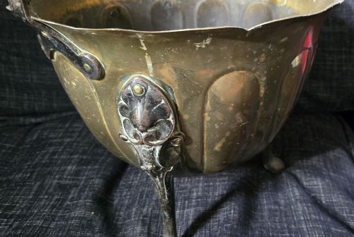 fig 4. An Arts and Crafts brass coal scuttle featuring a scalloped rim, vertical body fluting, three dark cast legs, and an overhead coiled handle.