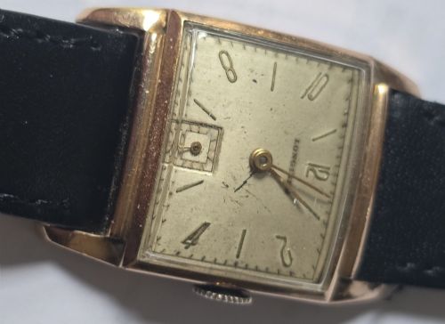 fig 12. A vintage Longines rectangular wristwatch featuring a rose gold-filled case, patinated dial with Arabic numerals, sub-seconds register, and a black leather strap.