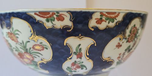 fig 3. An eighteenth-century circular porcelain bowl featuring a blue scale ground, gilded rococo cartouches, and hand-painted Kakiemon floral panels.