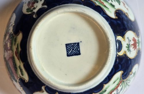 fig 5. An eighteenth-century circular porcelain bowl featuring a blue scale ground, gilded rococo cartouches, and hand-painted Kakiemon floral panels.
