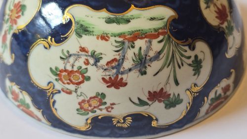 fig 7. An eighteenth-century circular porcelain bowl featuring a blue scale ground, gilded rococo cartouches, and hand-painted Kakiemon floral panels.