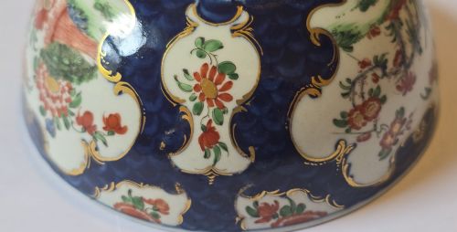fig 8. An eighteenth-century circular porcelain bowl featuring a blue scale ground, gilded rococo cartouches, and hand-painted Kakiemon floral panels.
