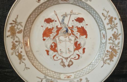 fig 1. A circular Chinese export porcelain plate featuring a central heraldic crest with red mantling, encircled by a geometric diaper border and floral sprigs.