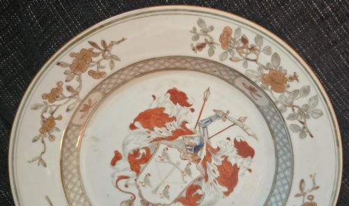 fig 4. A circular Chinese export porcelain plate featuring a central heraldic crest with red mantling, encircled by a geometric diaper border and floral sprigs.