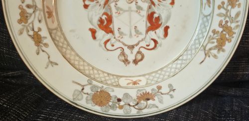 fig 5. A circular Chinese export porcelain plate featuring a central heraldic crest with red mantling, encircled by a geometric diaper border and floral sprigs.