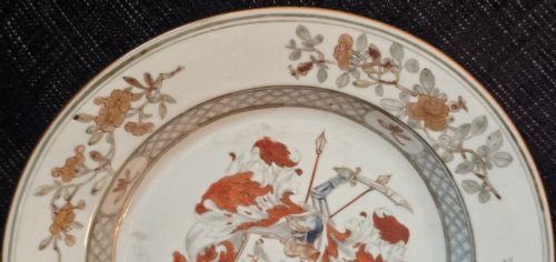 fig 6. A circular Chinese export porcelain plate featuring a central heraldic crest with red mantling, encircled by a geometric diaper border and floral sprigs.