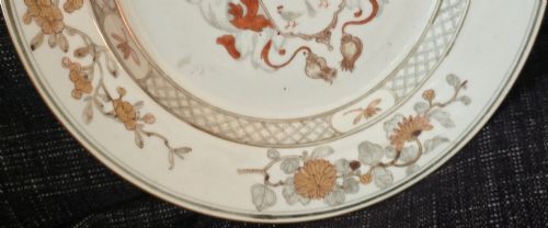 fig 7. A circular Chinese export porcelain plate featuring a central heraldic crest with red mantling, encircled by a geometric diaper border and floral sprigs.